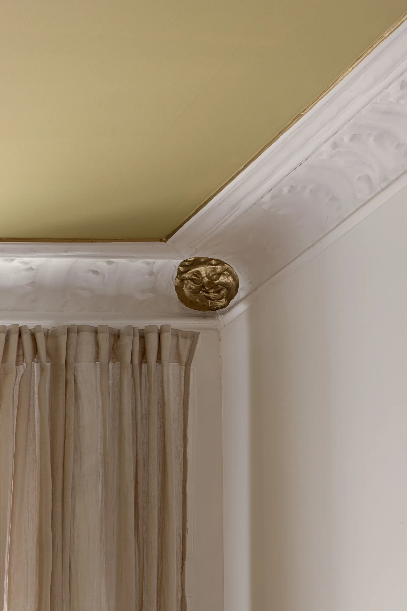 Ceiling detail at Alethia, Fiolstræde 14, Copenhagen: mustard ceiling, white stucco moulding and gilded face ornament above linen curtain