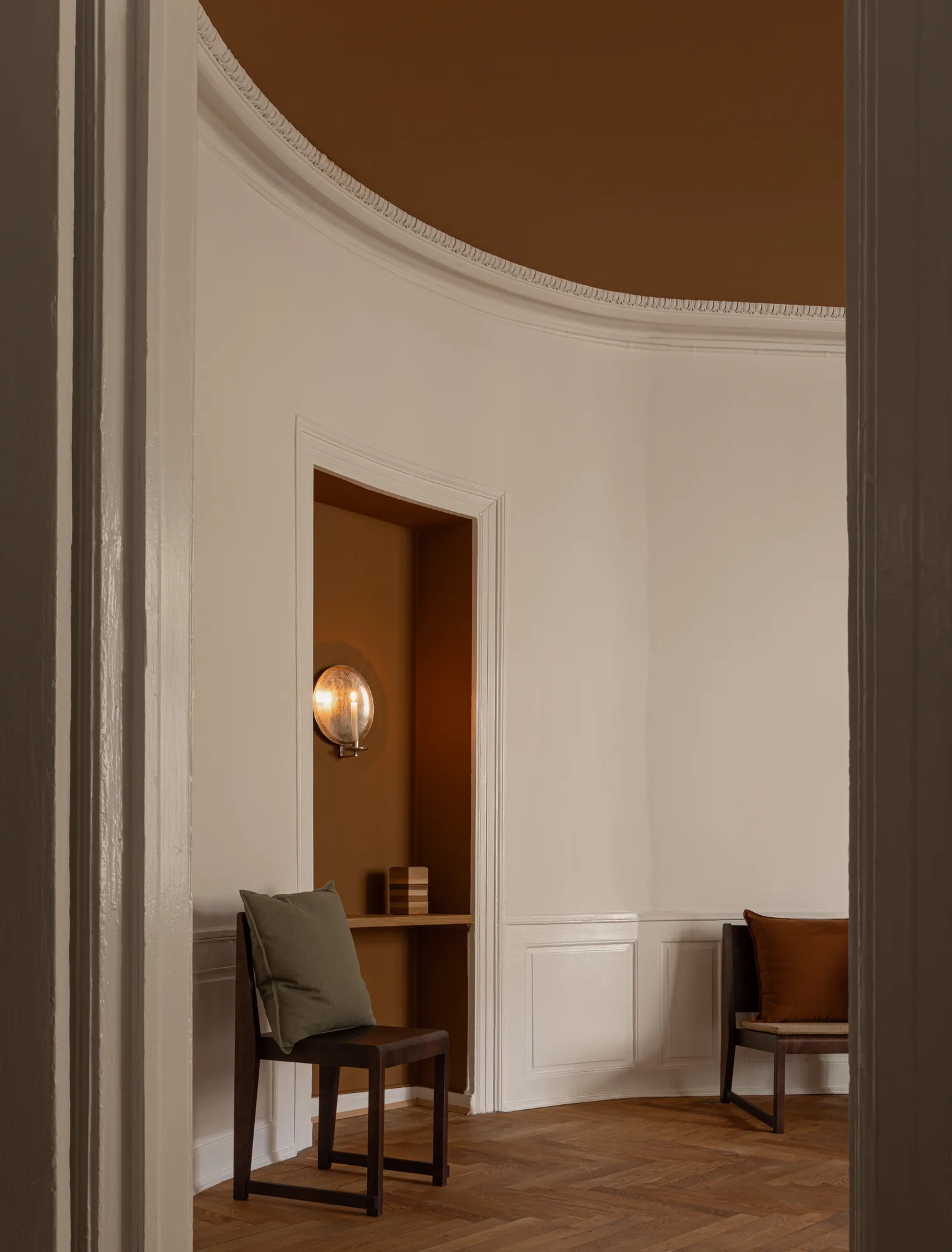 Curved-corner room in Alethia clinic, Fiolstræde 14, Copenhagen: vaulted stucco ceiling, doorway into a cognac alcove with wall sconce, dark wooden chairs