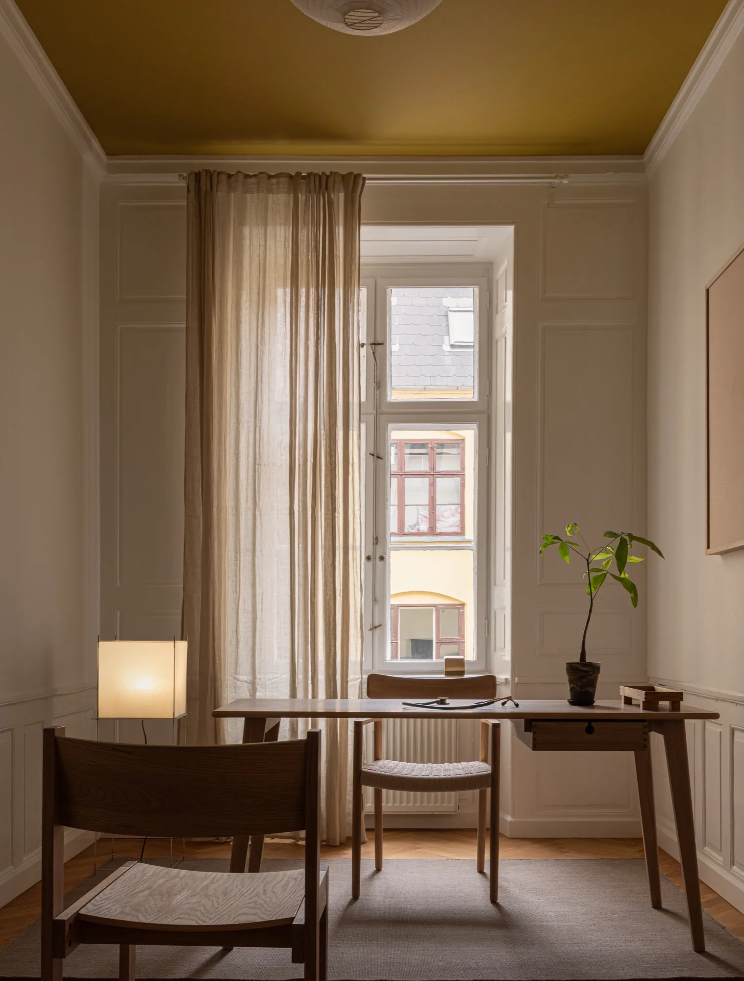 Consultation room at Fiolstræde 14: desk by the window with a lit table lamp and a plant